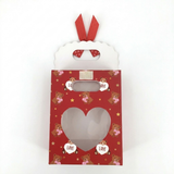Red gift bag with teddy bear pattern and heart cutout on a white background